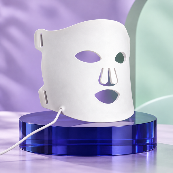 Máscara facial branca de LED flexível em pedestal azul com cenário violeta e menta